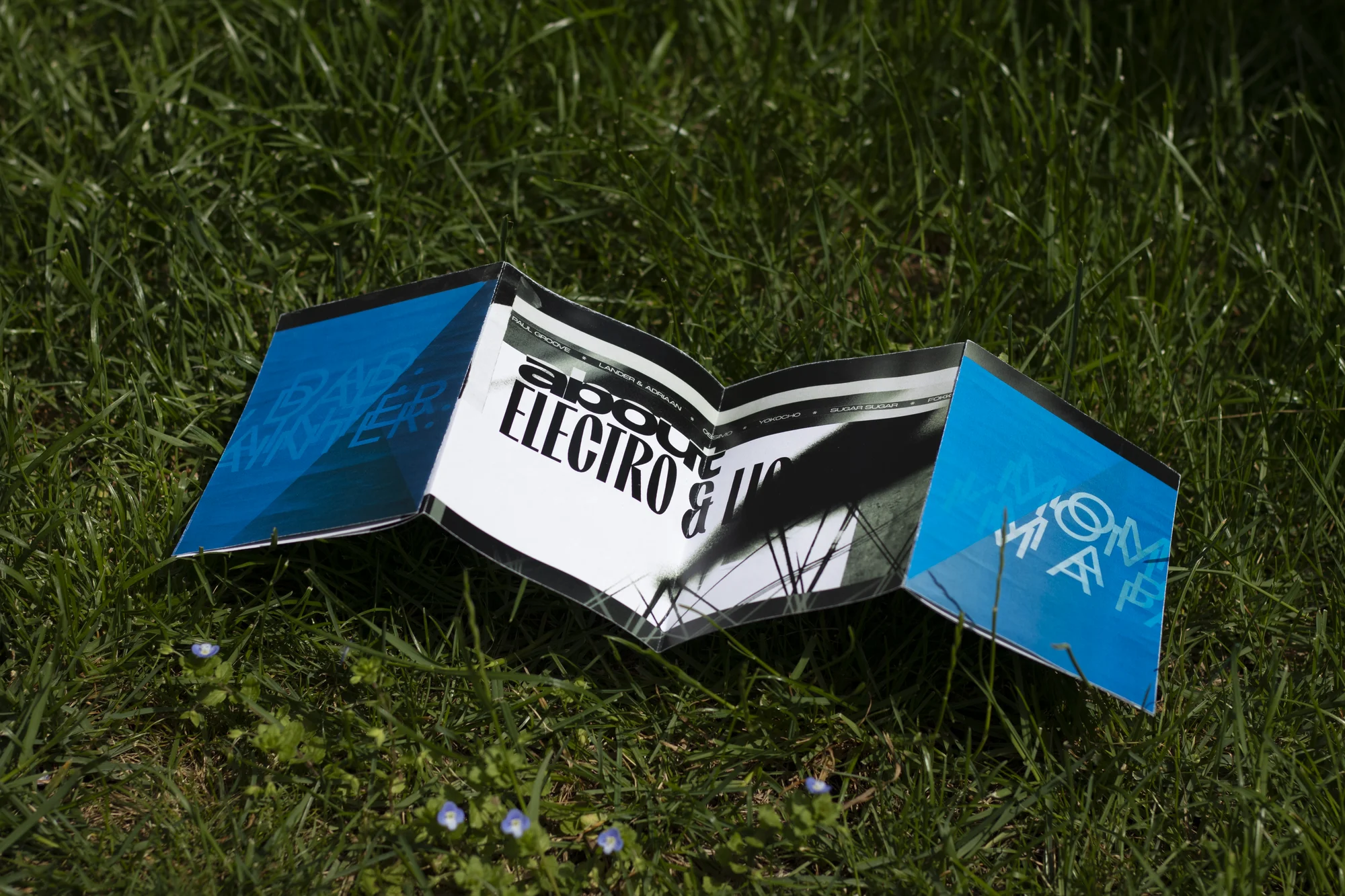 Vue globale du fanzine expérimental J'EXISTE posé sur l'herbe, révélant un design graphique audacieux en bichromie bleu et noir.